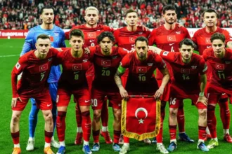A Milli Futbol Takımı oyuncuları sevinirken, arkada dünya ve Türkiye bayrakları görünüyor.